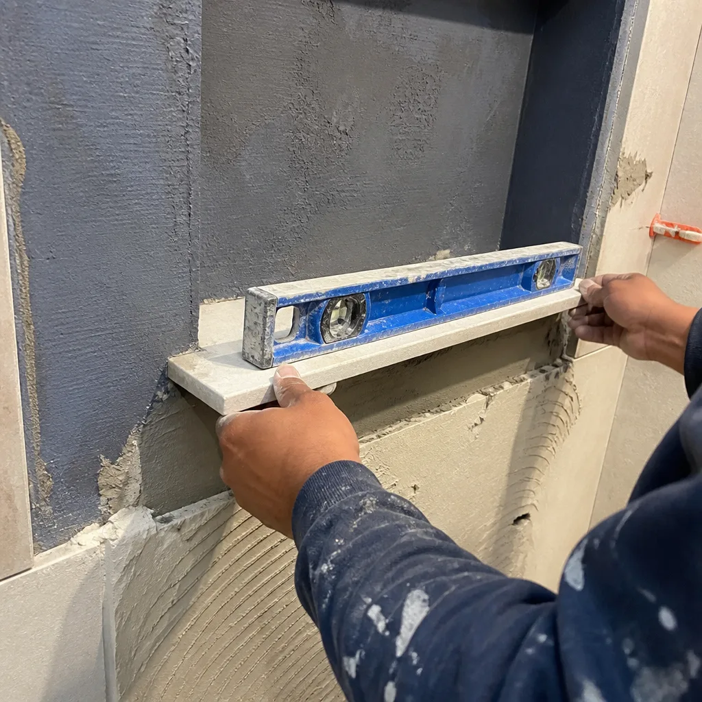 Contractor installing a stone shower niche shelf using a spirit level